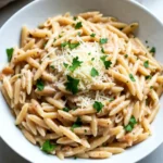 In this creamy garlic parmesan orzo dish, each ingredient plays a key role. Here's what you'll need: - 1 cup orzo pasta - 2 tablespoons extra virgin olive oil - 4 cloves garlic, finely minced - 1 cup vegetable broth (or chicken broth for added flavor) - 1 cup heavy cream - 1 cup freshly grated Parmesan cheese - 1 teaspoon Italian seasoning blend - Salt and freshly ground black pepper, to taste - Fresh parsley, finely chopped (for garnish) When choosing ingredients, I recommend using high-quality Parmesan cheese. Freshly grated cheese melts better and gives a rich flavor. For broth, you can use either vegetable or chicken. This choice can enhance the taste. Feel free to customize your dish! You can add cooked chicken or shrimp for a protein boost. Spinach or mushrooms can also add color and nutrition. Enjoy experimenting! {{ingredient_image_2}} To start, bring a medium saucepan filled with water to a rolling boil. Once boiling, add 1 cup of orzo pasta. Cook it according to the package instructions until it reaches al dente. This texture means the pasta is firm but not hard. After cooking, drain the pasta in a colander. Allow excess water to fully drain off. You want the orzo to be dry, so it absorbs the sauce well. Next, grab a large skillet. Heat 2 tablespoons of extra virgin olive oil over medium heat until it shimmers. Add 4 cloves of finely minced garlic. Sauté the garlic for about 1 minute. Watch it carefully; you don’t want it to burn. It should smell fragrant and turn lightly golden. Now, slowly pour in 1 cup of vegetable broth. Stir the mix well with a spatula. Let this come to a gentle simmer. Once it simmers, lower the heat. Gradually pour in 1 cup of heavy cream. Stir until everything blends nicely and heats through. After that, sprinkle in 1 cup of freshly grated Parmesan cheese. Keep stirring until the cheese fully melts. This creates a creamy sauce. Then, add 1 teaspoon of Italian seasoning blend. Season with salt and freshly ground black pepper to your taste. Taste the sauce and adjust if needed. Now it's time to bring it all together. Add the drained orzo to the skillet. Toss gently to coat every strand in the creamy sauce. This step is key; you want each bite to be rich and flavorful. For a beautiful finish, serve the dish hot. Garnish each serving with freshly chopped parsley. This adds color and a fresh touch. For an elegant presentation, consider serving the orzo in shallow bowls. Drizzle some extra virgin olive oil on top. You can also sprinkle more Parmesan and add a lemon wedge on the side for freshness. Enjoy your delightful dinner! To ensure the sauce thickens properly, keep the heat low when adding cream. Stir constantly to blend it well with the broth. Add the cheese gradually, allowing it to melt smoothly. This helps in creating a rich, creamy texture. If the sauce seems too thin, let it simmer a bit longer without the orzo. Adjusting seasoning is key to making this dish your own. Start with a pinch of salt and some black pepper. Taste frequently as you cook. If you want a kick, add more Italian seasoning or even a dash of crushed red pepper. Prep strategies can speed up your cooking time. Mince the garlic and measure out the cheese and other ingredients before you start. This way, you won’t waste time searching for items while cooking. For meal planning, you can make this dish ahead of time. Cook the orzo and sauce separately, then combine when you’re ready to serve. This lets you enjoy a quick meal on busy days. This creamy orzo pairs well with proteins like grilled chicken or sautéed shrimp. You can also serve it with a fresh salad or steamed vegetables. For an elegant presentation, serve the orzo in shallow bowls. Drizzle a bit of extra virgin olive oil on top. Sprinkle more grated Parmesan and add a sprig of parsley or a lemon wedge on the side. This makes the dish look as good as it tastes! Pro Tips Perfect Pasta Texture: Make sure to cook the orzo al dente, as it will continue to absorb sauce and cook slightly more once added to the skillet. Use Fresh Ingredients: Opt for freshly grated Parmesan cheese instead of pre-grated for a creamier texture and more robust flavor. Customize the Flavor: Feel free to add additional herbs like basil or thyme for an extra depth of flavor that complements the garlic and Parmesan. Make It a Meal: Add sautéed vegetables or cooked chicken to this orzo dish to turn it into a heartier main course. {{image_4}} You can change the pasta in this recipe. Use any small pasta you like. Farro, quinoa, or even rice can work well. For the cream, try using half-and-half or a non-dairy option. If you want more flavor, use chicken broth instead of vegetable broth. Adding proteins can make this dish heartier. Cooked chicken, shrimp, or even sautéed mushrooms fit perfectly. Just mix them in after adding the orzo. This adds great taste and makes it a full meal. Adding vegetables can boost flavor and nutrition. Spinach, peas, or mushrooms are great choices. Just sauté them with the garlic. This will give your dish a fresh taste and pop of color. You can also spice things up. Add Italian herbs like basil or oregano for a richer flavor. A pinch of red pepper flakes can add a nice kick. These tweaks will create layers of taste and keep your dinner exciting. To keep your creamy garlic Parmesan orzo fresh, store it in an airtight container. This helps preserve the creaminess. Let it cool to room temperature before sealing it. You can keep it in the fridge for up to three days. If you wait longer, it may lose its rich flavor and texture. When reheating, aim to keep the texture smooth and creamy. You can use the stovetop or microwave. For the stovetop, place the orzo in a skillet with a splash of broth or cream. Heat it on low, stirring often to prevent sticking. In the microwave, heat it in short bursts, stirring in between. This way, it heats evenly and stays delicious. Yes, you can make Creamy Garlic Parmesan Orzo gluten-free. Use gluten-free orzo pasta. Many brands offer great options made from rice or corn. You can find these at most grocery stores. Just follow the cooking instructions on the package. To make this dish vegetarian-friendly, choose vegetable broth instead of chicken broth. This keeps the flavor rich. You can also add more veggies for extra nutrition. Try spinach, cherry tomatoes, or mushrooms. These will boost taste and color. This orzo pairs well with many side dishes. Consider a fresh garden salad or steamed vegetables. Grilled chicken or shrimp can add protein. For drinks, a light white wine or sparkling water works well. These options bring balance to the meal. This blog post covered all the steps to make a delicious creamy garlic Parmesan orzo. We discussed key ingredients, preparation tips, and serving ideas. You now have methods to customize your dish and store leftovers. Remember, great cooking is about adjusting flavors and making it your own. Use what you love and don’t shy away from experimenting. Enjoy every bite of your creamy creation!