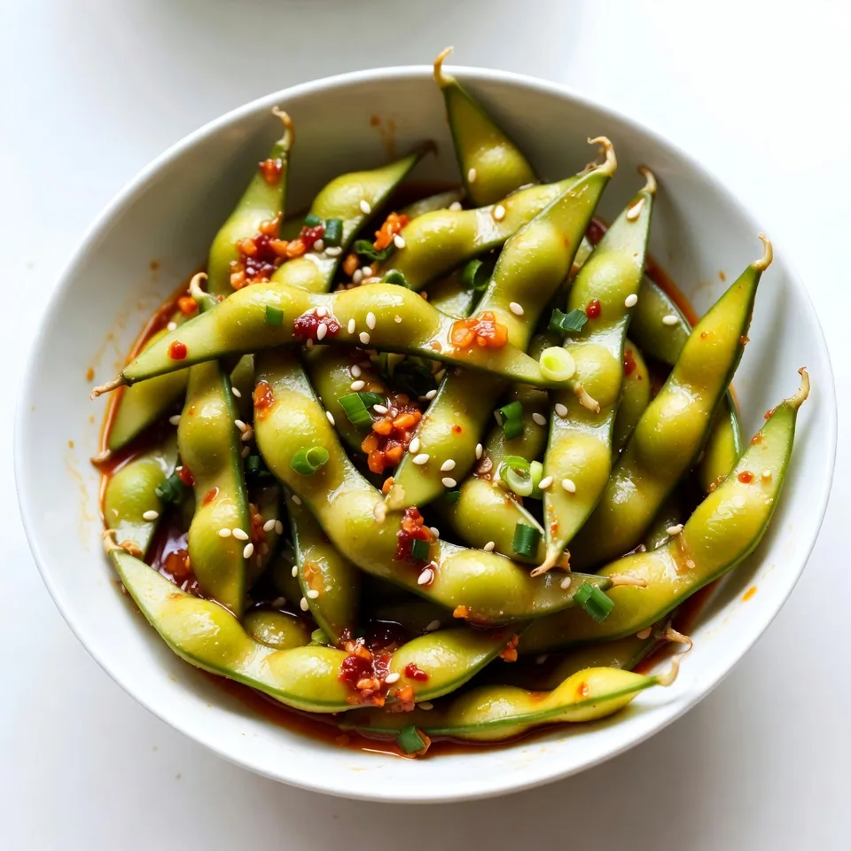 - 2 cups edamame in pods (fresh or frozen) - 3 tablespoons high-quality olive oil - 4 cloves garlic, finely minced - 1-2 tablespoons chili paste (adjust based on desired heat level) - 1 tablespoon soy sauce - 1 teaspoon toasted sesame oil - 1/2 teaspoon sea salt - 1 tablespoon sesame seeds - Chopped green onions for garnish (optional) I love using fresh or frozen edamame for this snack. The bright green pods add color and flavor to any meal. Olive oil is my go-to for cooking. It gives a nice richness that makes everything taste great. Garlic brings a strong, warm taste that pairs well with edamame. I use four cloves, but you can add more if you love garlic. Chili paste adds heat. You can adjust how much you use based on how spicy you want it. Soy sauce gives a salty, umami flavor. Toasted sesame oil adds a nutty touch. Sprinkle sea salt for extra seasoning. Finally, sesame seeds and green onions make the dish look nice. These ingredients come together to make spicy garlic edamame a tasty and quick snack. {{ingredient_image_2}} Cooking fresh edamame: To cook fresh edamame, bring a pot of salted water to a boil. Add the edamame pods. Cook them for about 5-6 minutes. They should feel tender but remain bright green. After cooking, drain them and set aside. Cooking frozen edamame: If you use frozen edamame, just follow the package instructions. Usually, you’ll boil or steam them until tender. Once they are cooked, drain and set aside. Heating the olive oil: In a large skillet, pour in 3 tablespoons of olive oil. Set the heat to medium. Wait until the oil shimmers, which shows it’s ready for the next step. Sautéing the garlic: Add 4 cloves of finely minced garlic to the hot oil. Stir frequently for 1-2 minutes. You want the garlic to be fragrant and lightly golden. Be careful not to burn it, as burnt garlic can ruin the flavor. Adding chili paste and soy sauce: Once the garlic is aromatic, it’s time to add flavor. Stir in 1-2 tablespoons of chili paste and 1 tablespoon of soy sauce. Mix well to create a spicy garlic sauce. Tossing in the edamame: Now, add the cooked edamame pods to the skillet. Toss them in the sauce. Make sure every pod is well-coated. Stir-fry for 3-4 minutes. This allows the flavors to blend perfectly. Adding sesame oil and sea salt: Drizzle 1 teaspoon of toasted sesame oil over the edamame. Sprinkle with 1/2 teaspoon of sea salt. Give everything a final toss to mix. Garnishing with sesame seeds and green onions: Remove the skillet from heat. Transfer the edamame to a serving bowl. If you want, sprinkle 1 tablespoon of sesame seeds and some chopped green onions on top. This adds a nice touch and crunch. - Choosing the right olive oil: Use a high-quality olive oil. It adds great flavor. Look for extra virgin oil. It has the best taste and health benefits. A good brand makes a big difference. - Not burning the garlic: Keep an eye on the garlic. It cooks fast and can burn easily. Stir it often and watch for a light golden color. Burned garlic tastes bitter, and we don't want that. - Adjusting heat level with chili paste: Start with one tablespoon of chili paste. Taste it, then add more if you want more heat. You control the spice. This recipe can be mild or fiery based on your choice. - Additional toppings for extra flavor: Consider adding toppings like sesame seeds or green onions. They add crunch and color. You can also try crushed red pepper or a squeeze of lime for a fresh kick. These small touches elevate your dish. Pro Tips Fresh vs. Frozen Edamame: If possible, opt for fresh edamame as it tends to have a better texture and flavor. Frozen edamame works as a great time-saver, just ensure it is cooked properly. Adjusting Spice Levels: Start with 1 tablespoon of chili paste if you're unsure about the heat. You can always add more later, but it's difficult to reduce spice once it's in the dish. Perfect Garlic Sauté: Keep an eye on the garlic while sautéing. It should be fragrant and lightly golden, but not burnt, as burnt garlic will impart a bitter taste to your dish. Serving Suggestions: Consider pairing your edamame with a refreshing drink like iced tea or a light beer to balance the spiciness and enhance your snacking experience. {{image_4}} You can adjust the spiciness of your edamame to fit your taste. For a mild version, use less chili paste. Start with just one tablespoon and taste. This way, you keep the garlic flavor strong without too much heat. If you love spicy food, try an extra spicy version. Add two tablespoons of chili paste. You can even mix in some red pepper flakes for a kick. Just be careful, as too much heat can overpower the dish. You can easily swap some ingredients for different flavors. For a healthier option, use avocado oil instead of olive oil. It has a mild taste and is rich in good fats. If you want a vegetarian option, use tamari instead of soy sauce. Tamari is gluten-free and has a rich flavor. It works well in this recipe, keeping the essence intact. Experimenting with these variations can help you find your perfect spicy garlic edamame! To keep your spicy garlic edamame fresh, store it right. First, let it cool to room temperature. Place the edamame in an airtight container. This helps lock in moisture and flavor. You can keep it in the fridge for up to three days. If you want to keep it longer, consider freezing it. To freeze, spread the cooled edamame in a single layer on a baking sheet. Once frozen, transfer it to a freezer-safe bag. This way, you can enjoy this tasty snack later. When you are ready to enjoy your edamame again, reheat it carefully. The microwave works well for this. Place the edamame in a microwave-safe bowl. Add a splash of water to keep it moist. Cover the bowl with a microwave-safe lid or wrap. Heat in short bursts, about 30 seconds at a time. Stir and check the edamame until warm. You can also reheat it in a skillet. Just add a little olive oil over medium heat. Stir gently until warmed through, and it will taste great again. Edamame are young soybeans. They grow in pods and are popular in many dishes. They are often served as a snack or appetizer. Edamame is packed with protein, fiber, and vitamins. This makes them a great healthy choice. One cup of edamame provides about 17 grams of protein. They also have antioxidants and help with heart health. Yes, you can use other legumes if needed. Some good substitutes are green peas, black beans, or chickpeas. Each offers a different taste and texture. Green peas are sweet and tender. Black beans give a rich flavor. Chickpeas provide a nice bite. You can adapt your sauce to match these legumes. Cooking time varies based on the type of edamame. Fresh edamame takes about 5-6 minutes in boiling water. Frozen edamame usually needs around 4-5 minutes. Always check the package for specific instructions. Both options should be tender but still bright green. This helps keep their flavor and nutrients. In this blog post, I shared a simple recipe for making a tasty edamame dish. We discussed ingredients, cooking steps, and helpful tips to enhance flavor. Remember to adjust the chili paste for your preferred spice level. You can also try substitutions if needed. Whether for a snack or a side, this recipe is quick and easy. Enjoy making your edamame dish, and don’t hesitate to experiment for your perfect flavor!